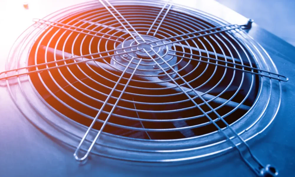 Close-up of residential air conditioning unit fan and condenser coils with orange heat effect showing cooling system operation