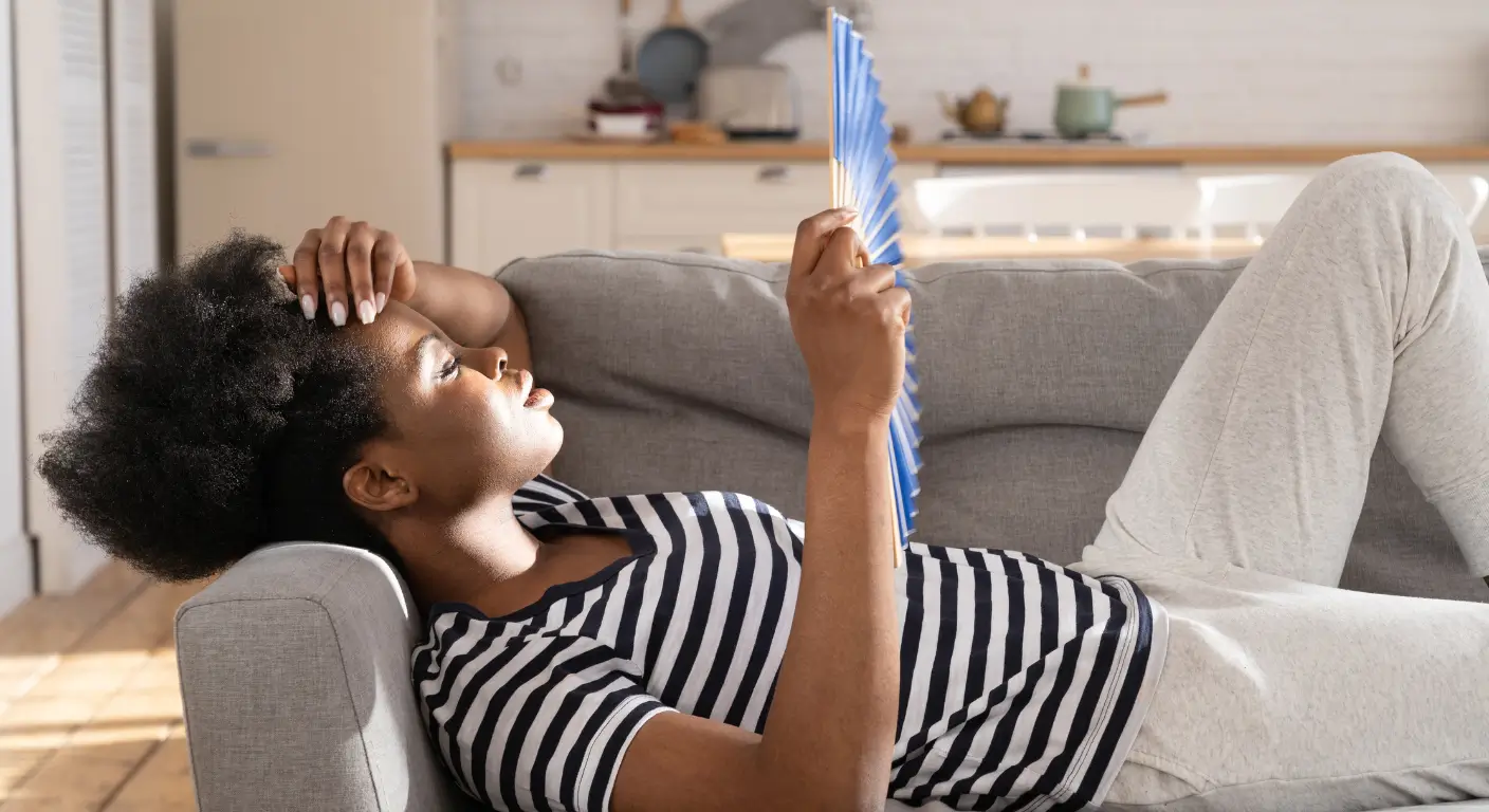 Woman using handheld fan on couch while air conditioner won't turn on in New Orleans home - emergency cooling needed
